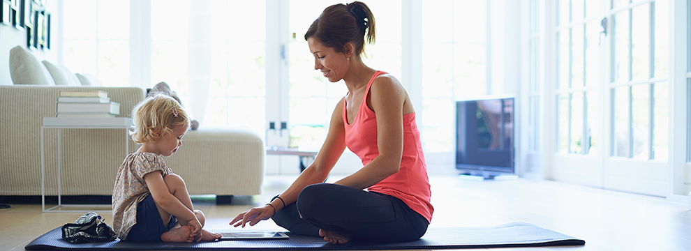Mother and toddler daughter sitting on a yoga mat