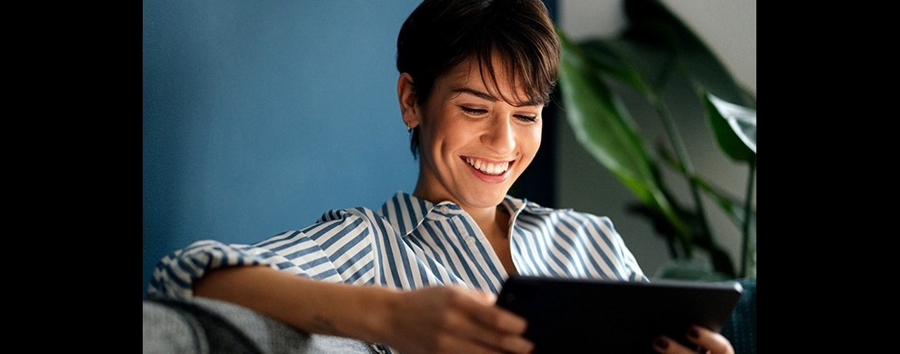Woman wearing a stripy shirt sitting on a grey couch using an iPad